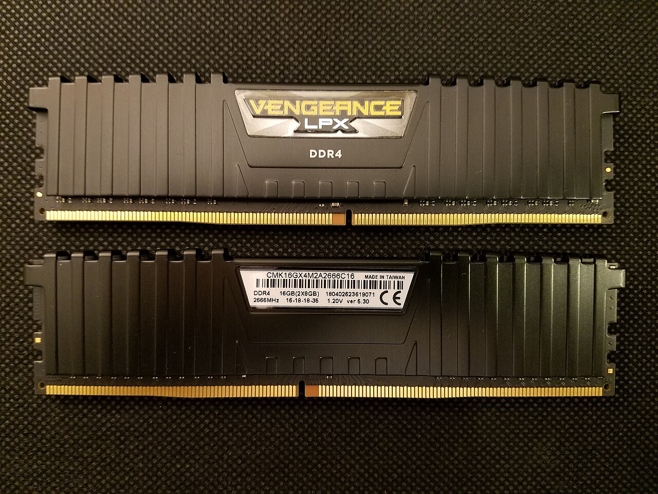 Dos módulos de memoria Corsair Vengeance LPX DDR4 sobre una superficie oscura; en el segundo se lee la etiqueta blanca con el código CMK16GX4M2A2666C16, 16 GB en dos módulos de 8 y 2666 MHz